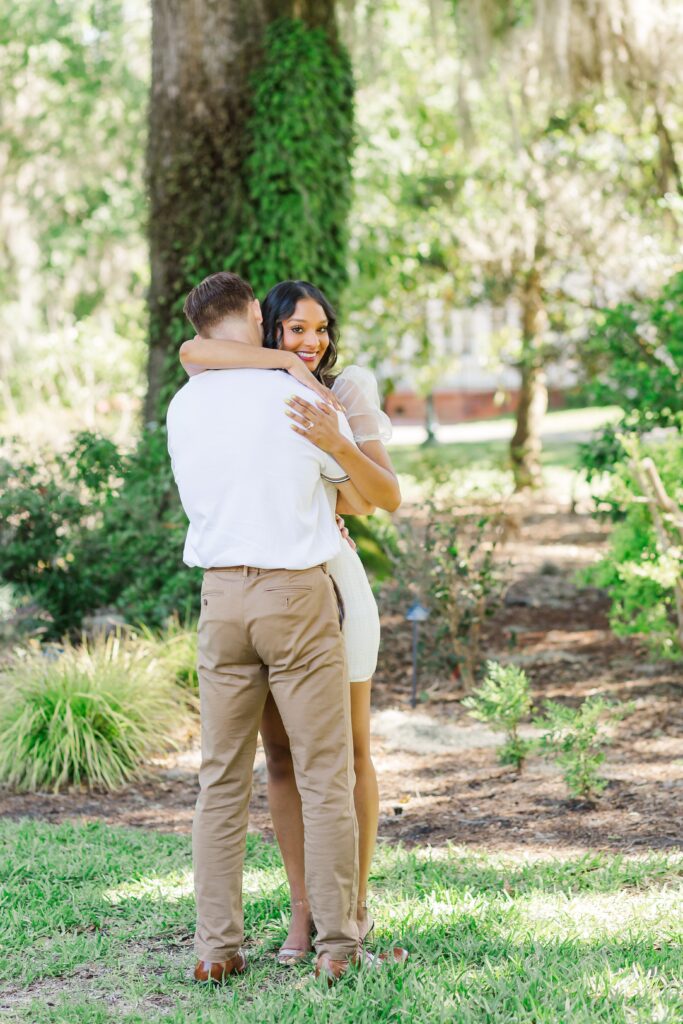 Girl hugs guy in front of large tree with hanging moss for their engagement photos at Leu Gardens in Orlando, Florida