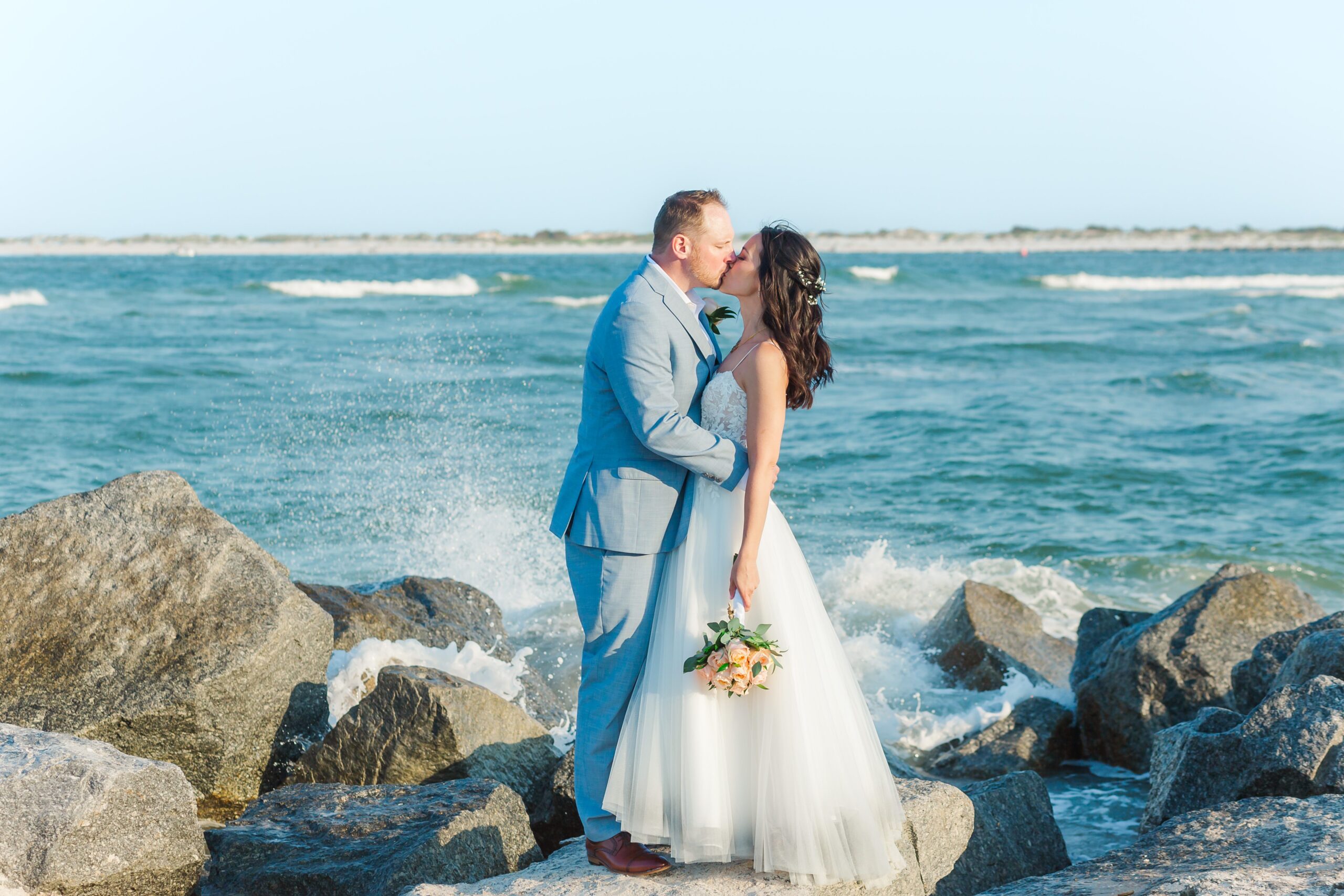 Bride and Groom kiss as they stand on rocks from the jetty at Vilano Beach for their St. Augustine beach wedding