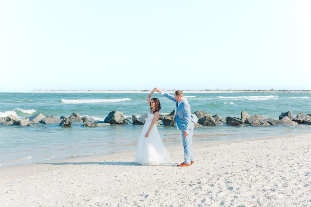 Groom twirls Bride as they stand in front of rocks from the jetty at Vilano Beach for their St. Augustine beach wedding