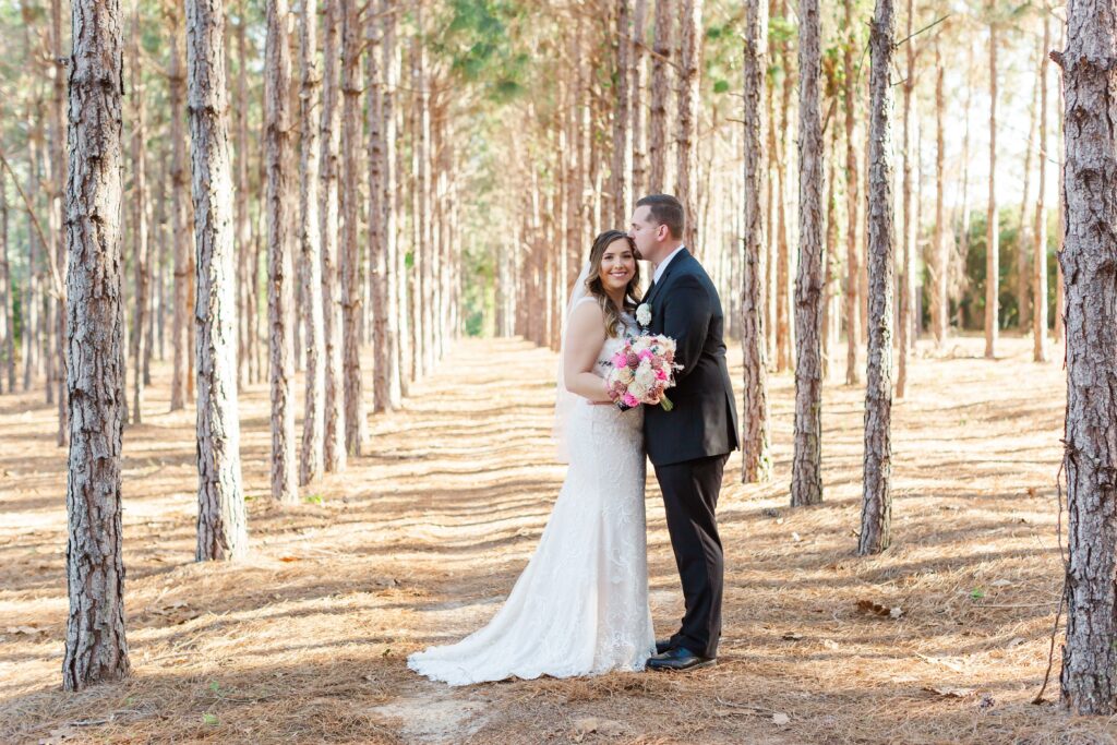 Groom kisses Bride's forehead under pine trees for their forest wedding at The Pinery Orlando in Howey in the Hills, FL
