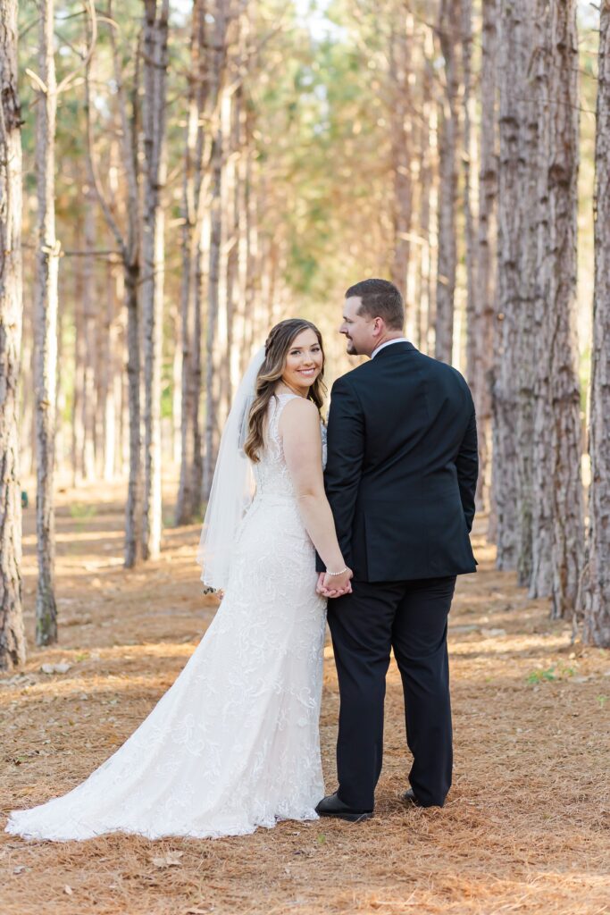Bride and Groom hold hands under pine trees for their forest wedding at The Pinery Orlando in Howey in the Hills, FL