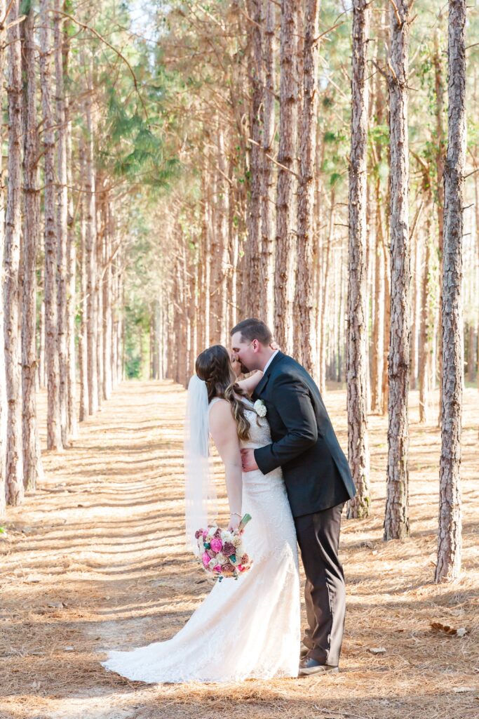 Groom dips and kisses Bride under pine trees for their forest wedding at The Pinery Orlando in Howey in the Hills, FL