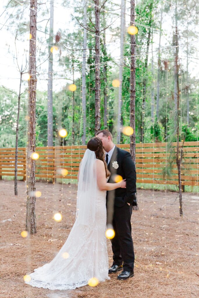 Bride and Groom kiss under twinkle lights and pine trees for their Forest Wedding at the Pinery Orlando Wedding and Events at Howey in the Hills, FL