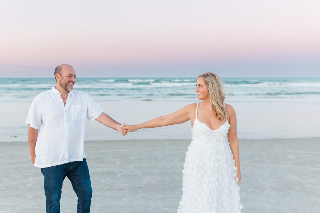 Couple walks and holds hands on the beach at sunset for their anniversary photos with their New Smyrna Beach Photographer