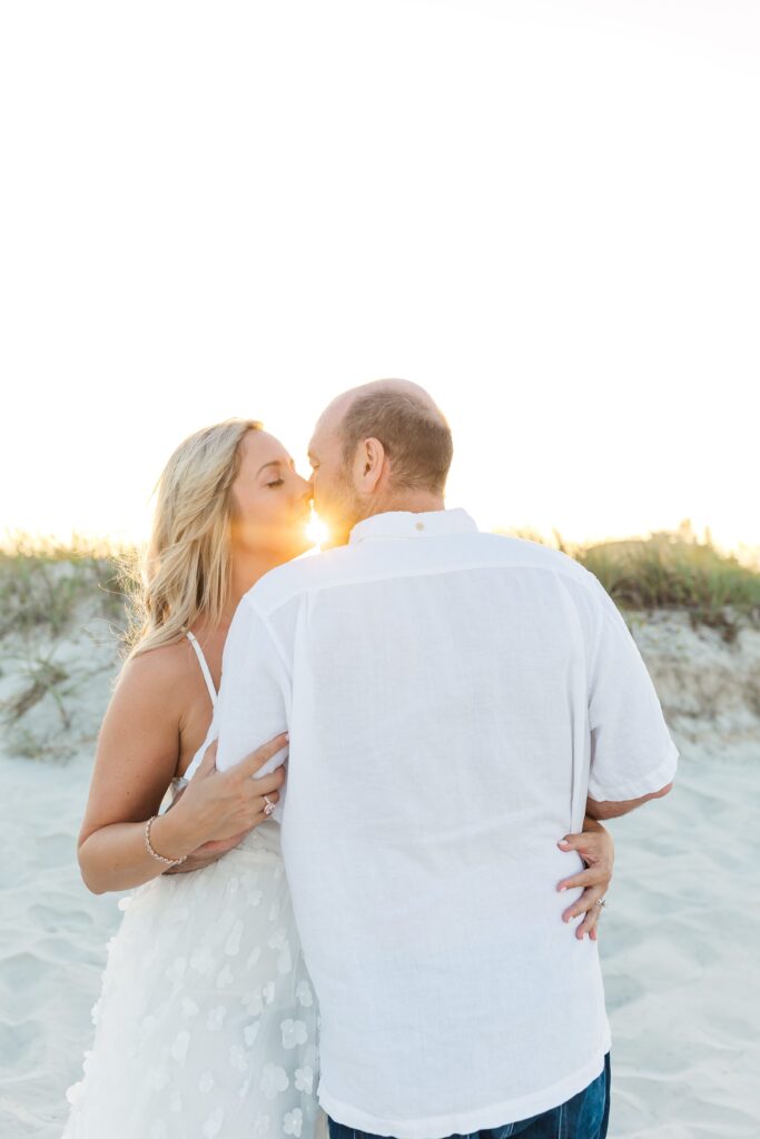 Couple kisses in the sand dunes with the sunset in the background for their anniversary photos with their New Smyrna Beach Photographer