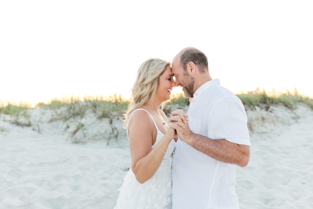 Couple holds hands looking at each other in the sand dunes for their anniversary photos with their New Smyrna Beach Photographer