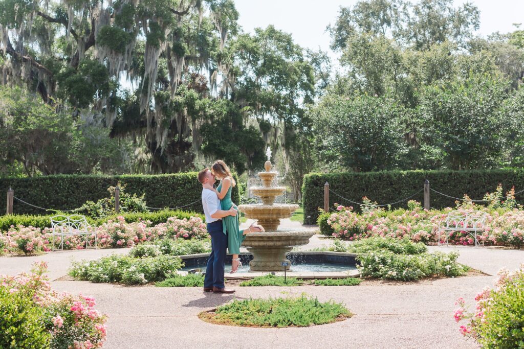 Guy lifts and kisses girl as they stand in front of fountain in the rose garden for their engagement photos at Leu Gardens Orlando