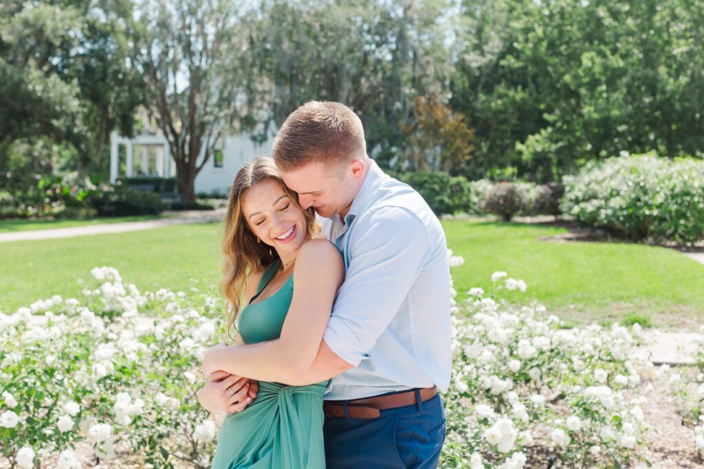 Guy snuggles girl as they stand in the rose garden for their engagement photos at Leu Gardens Orlando