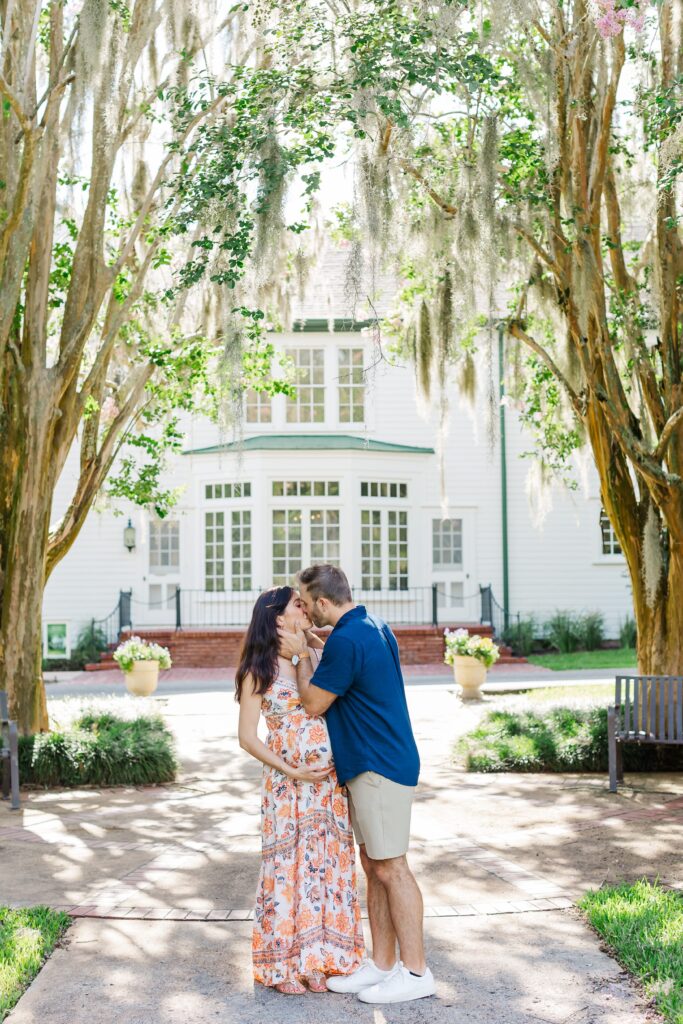 Couple kisses large trees with hanging moss for their Orlando Maternity Photos at Leu Gardens