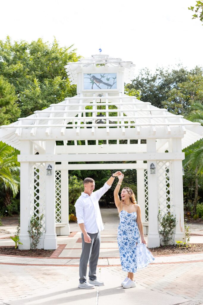 Guy twirls girl for their engagement photos in the idea garden at Leu Botanical Garden in Orlando, Florida
