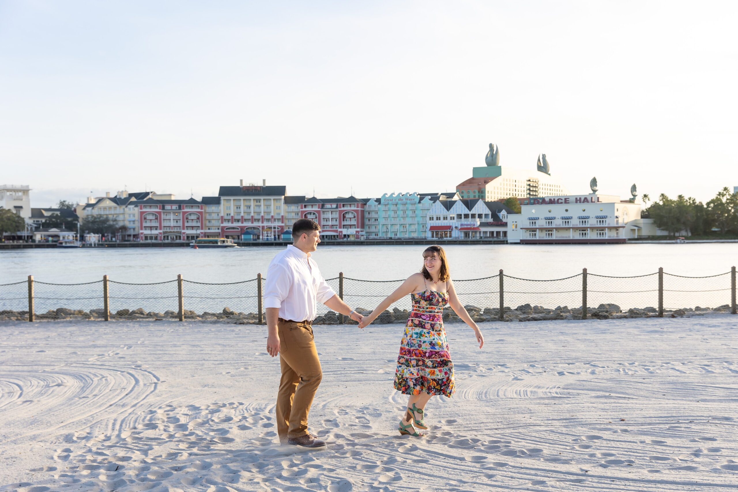 Couple holds hands and walks along the beach at Disney's Beach Club Resort for their engagement photos