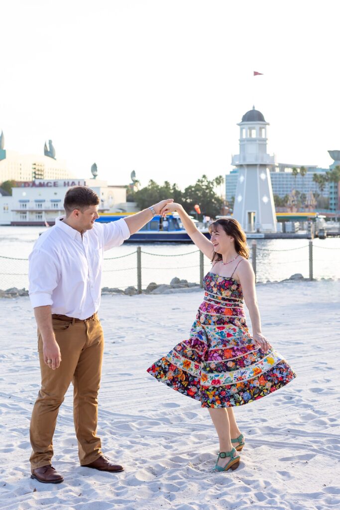 Guy twirls girl in front of lighthouse on the beach at Disney's Beach Club Resort for their engagement photos