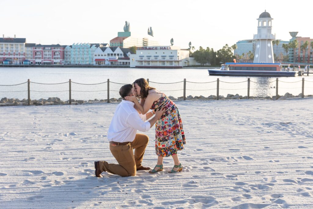 Girl kisses guy after he proposes in front of lighthouse on the beach at Disney's Beach Club Resort for their engagement photos