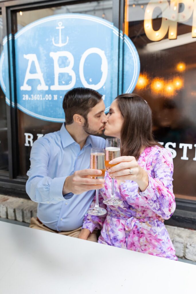 Couple kisses with champagne toast for their engagement photos at Atlantic Beer and Oyster on Park Ave in Winter Park, Florida