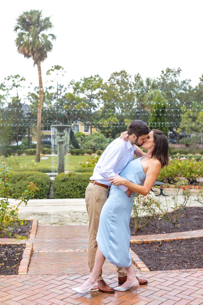 Guy dips and kisses girl in front of peacock fountain for their engagement photos on Park Ave in Winter Park, Florida