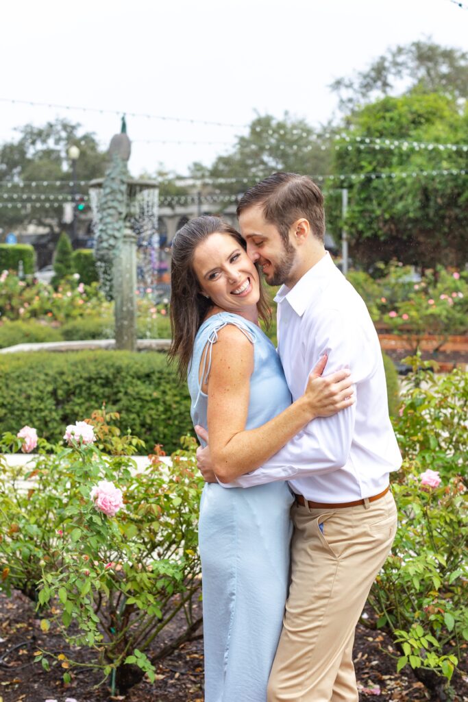 Couple smiles and snuggles in front of peacock fountain for their engagement photos on Park Ave in Winter Park, Florida