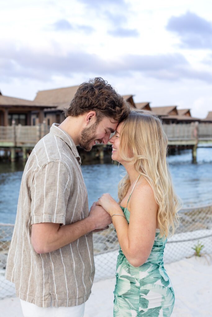 Couple holds hands and smiles on the beach after their proposal at Disney's Polynesian Resort in Orlando, Florida