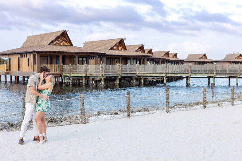 Couple kisses on the beach after their proposal in front of the bungalows at Disney's Polynesian Resort in Orlando, Florida