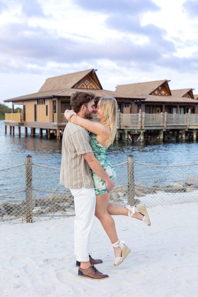 Guy lifts girl on the beach after their proposal in front of the bungalows at Disney's Polynesian Resort in Orlando, Florida