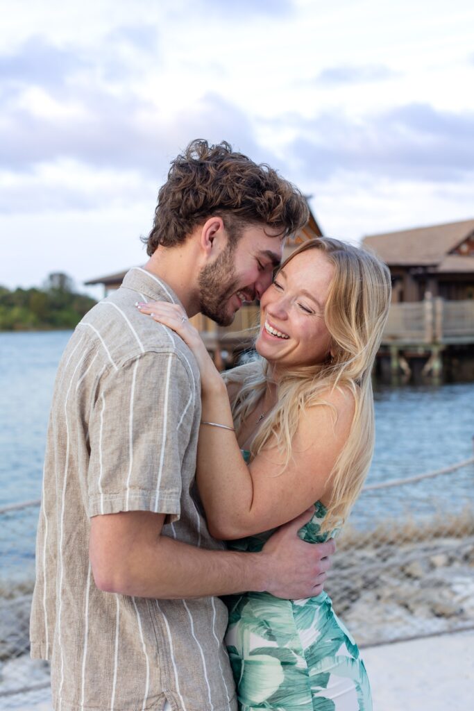 Couple snuggles and laughs on the beach after their proposal in front of the bungalows at Disney's Polynesian Resort in Orlando, Florida