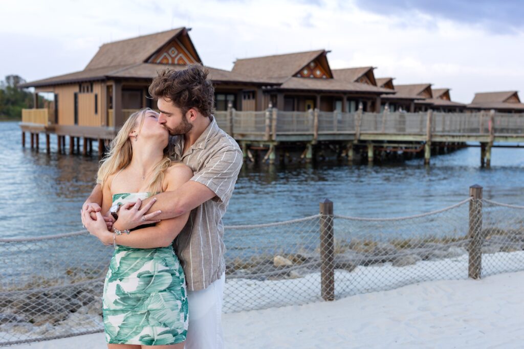 Couple kisses on the beach after their proposal in front of the bungalows at Disney's Polynesian Resort in Orlando, Florida