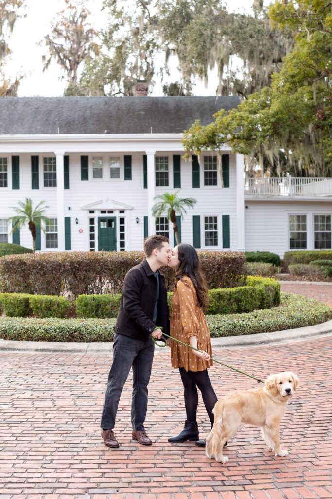 Couple walks with their dog in front of Cypress Grove Estate House for their engagement photos at Cypress Grove Park in Orlando, Florida