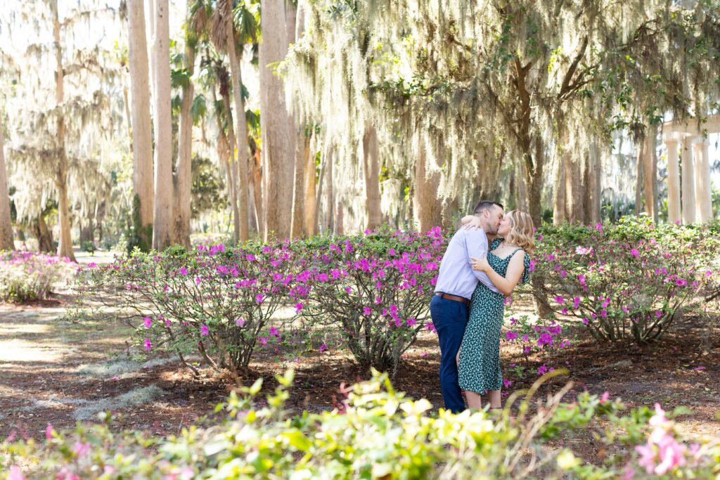 Couple kisses in front of purple azaleas for their engagement photos at Kraft Azalea Garden in Orlando, Florida