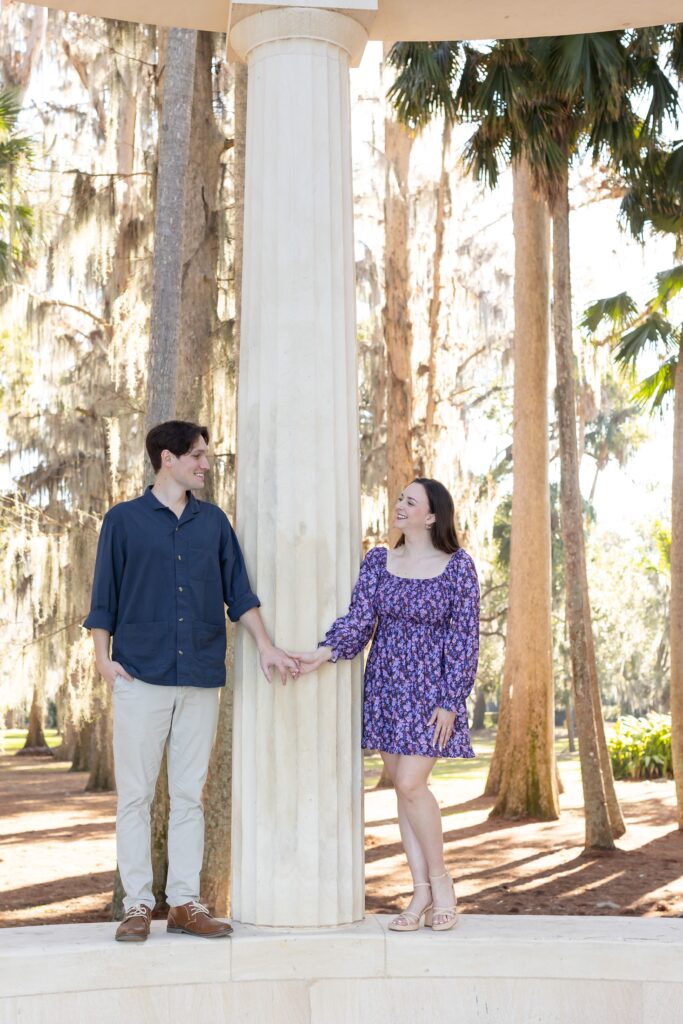 Couple holds hands on top of columns for their engagement photos at Kraft Azalea in Orlando, Florida