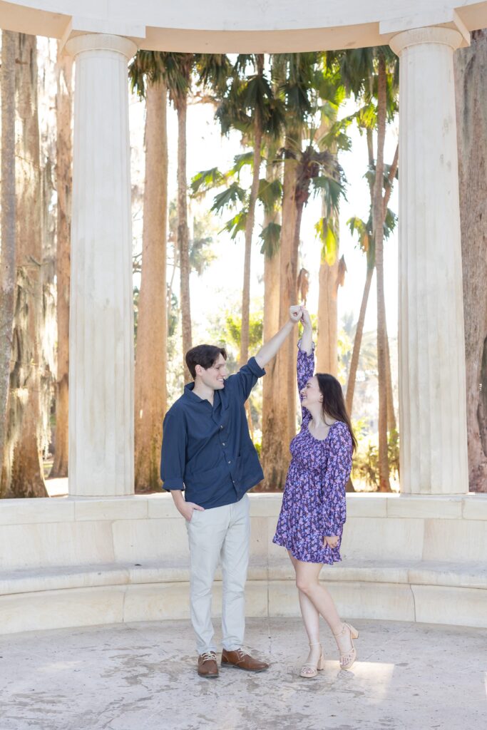 Guy twirls girl in front of columns for their engagement photos at Kraft Azalea in Orlando, Florida