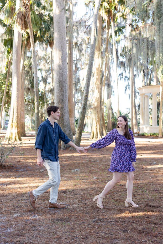 Couple laughs and holds hands while they walk for their engagement photos at Kraft Azalea in Orlando, Florida