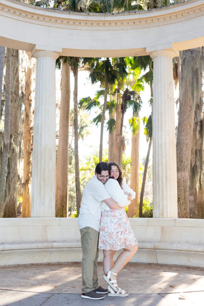 Couple hugs under the columns for their engagement photos at Kraft Azalea Garden in Winter Park, Florida