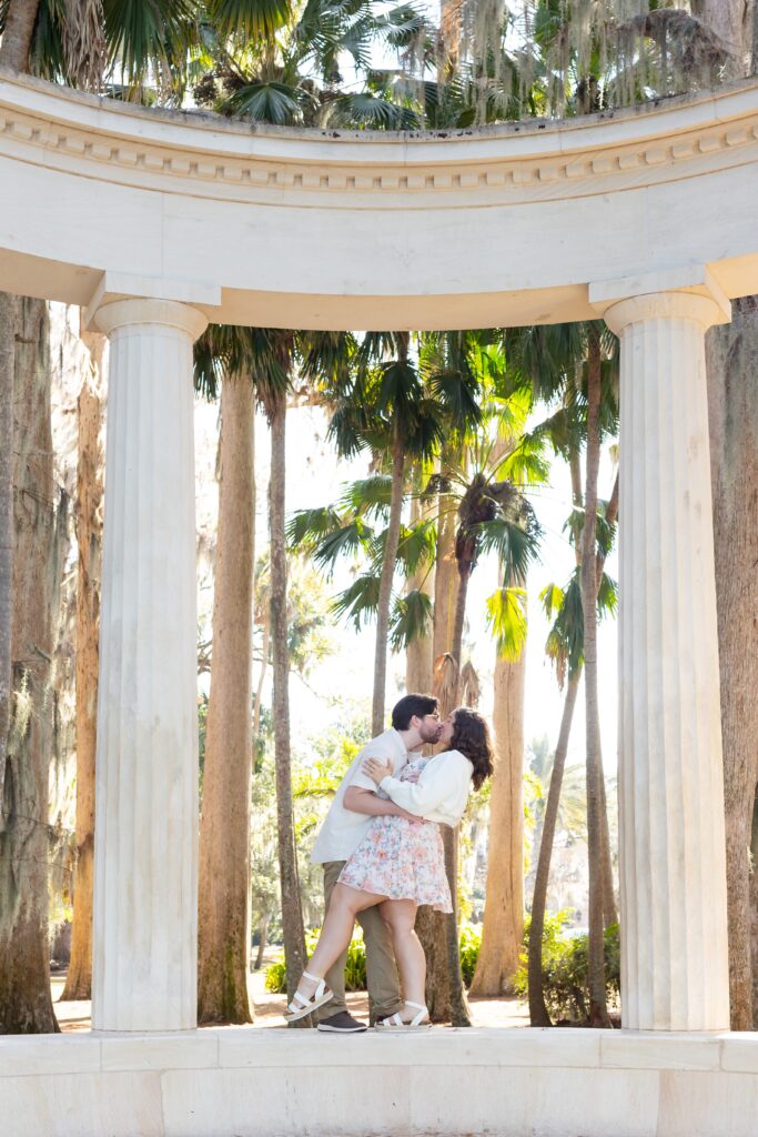 Guy dips and kisses girl under the columns for their engagement photos at Kraft Azalea Garden in Winter Park, Florida