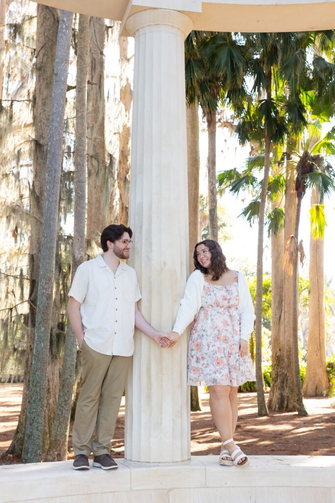 Couple holds hands by the columns for their engagement photos at Kraft Azalea Garden in Winter Park, Florida