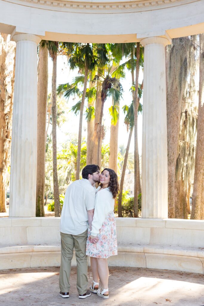 Couple holds hands and stands under the columns for their engagement photos at Kraft Azalea Garden in Winter Park, Florida