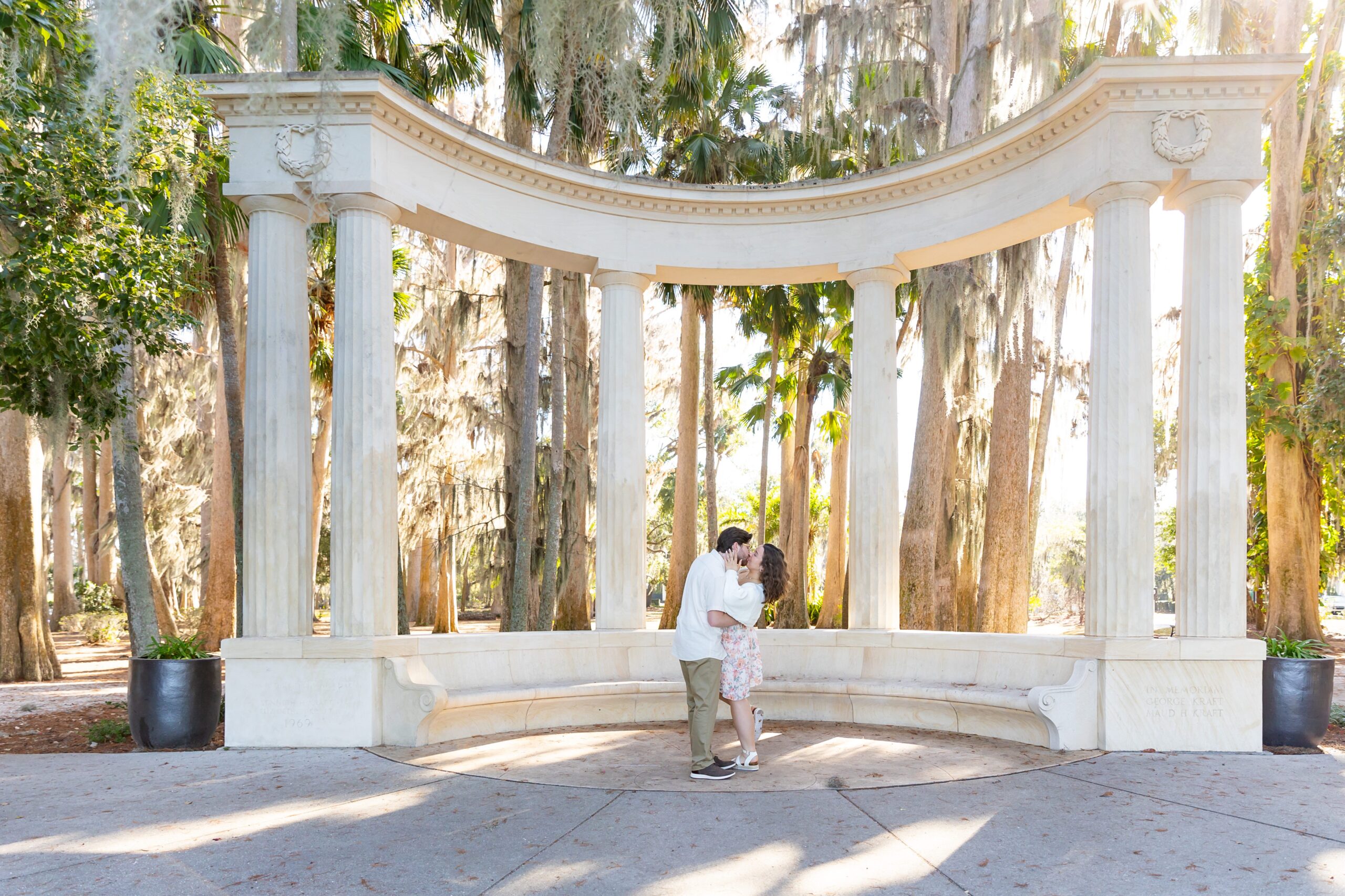 Couple kisses under the columns for their engagement photos at Kraft Azalea Garden in Winter Park, Florida