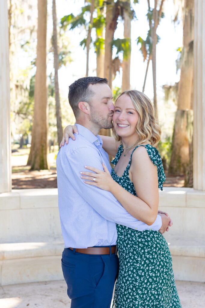 Guy kisses girls cheek in front of columns for their engagement photos at Kraft Azalea Garden in Orlando, Florida