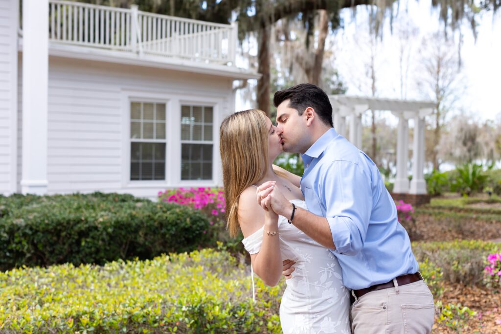 Couple holds hands and kisses in front of purple flowers for their engagement photos at Cypress Grove Park in Orlando, Florida