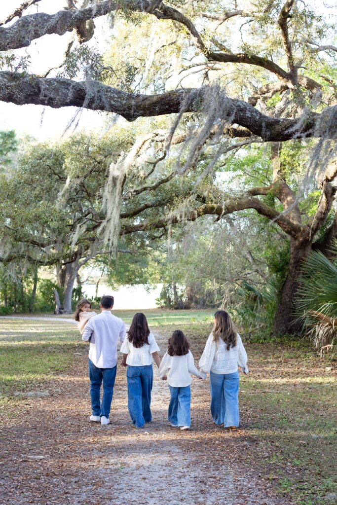 Family walking and holding hands under spanish moss tree for their family photos at Greenwood Lakes Park in Lake Mary, Florida with Orlando Family Photgrapher Amy Britton Photography