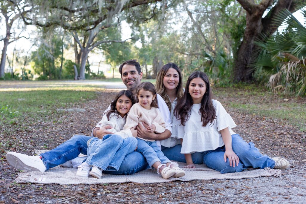 Family poses on blanket under spanish moss tree for their family photos at Greenwood Lakes Park in Lake Mary, Florida with Orlando Family Photgrapher Amy Britton Photography