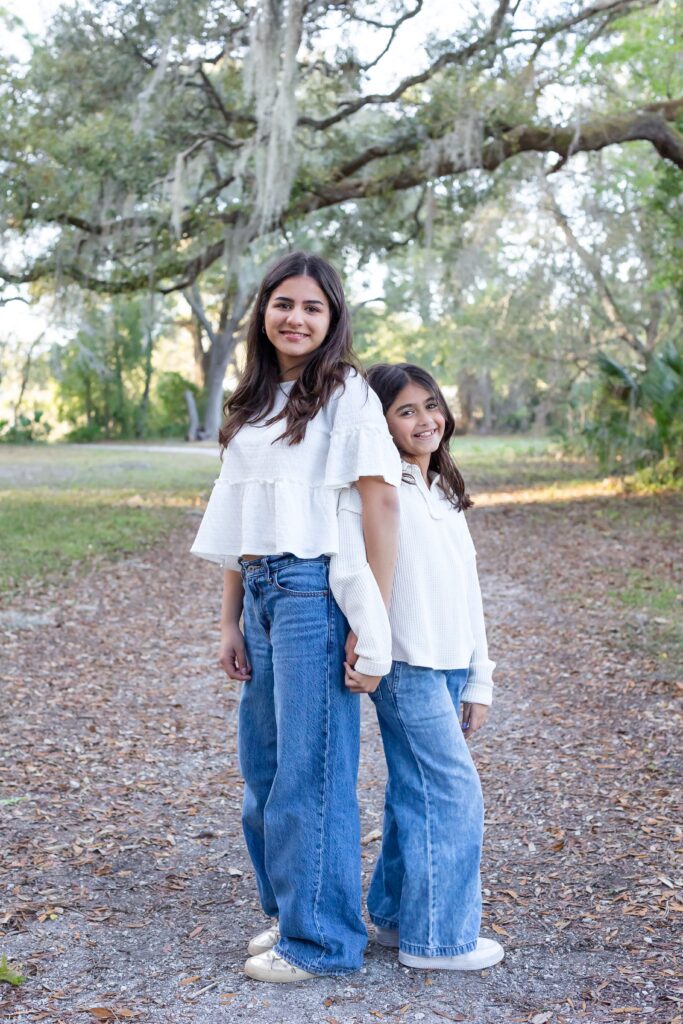 Sisters stand back to back for their family photos at Greenwood Lakes Park in Lake Mary, Florida with Orlando Family Photgrapher Amy Britton Photography