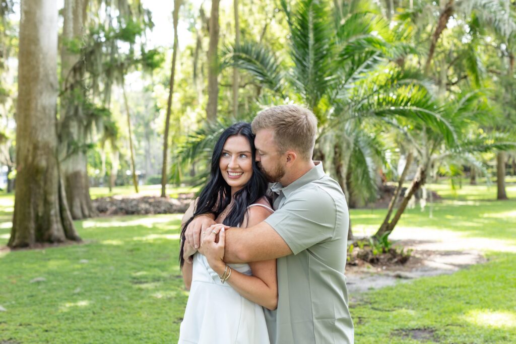 Guy hugs and kisses girls cheek in front of palm trees at Kraft Azalea Park in Winter Park, Orlando, Florida