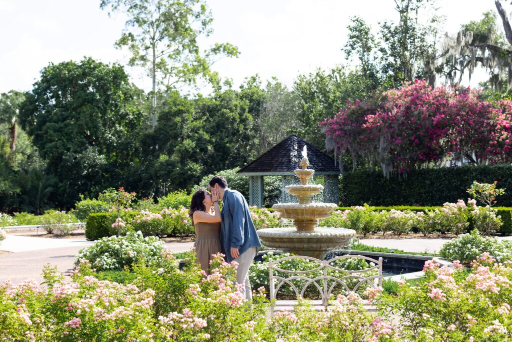 Couple kisses in front of rose garden fountain for their engagement photos at Leu Gardens in Orlando, Florida