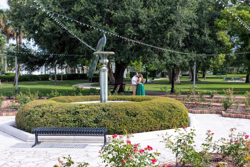 Couple kisses in front of the peacock fountain at Rose Garden in Central Park Winter Park, Florida