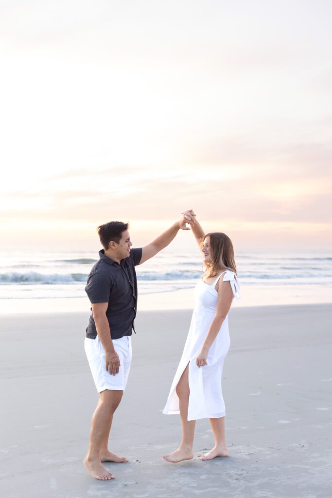 Guy twirls girl on the beach at sunrise for their engagement photos at New Smyrna Beach, Florida