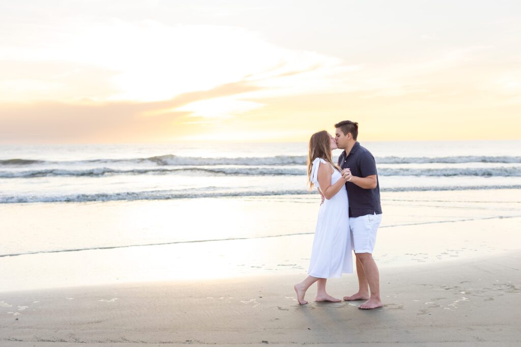 Couple kisses on the beach at sunrise for their engagement photos at New Smyrna Beach, Florida