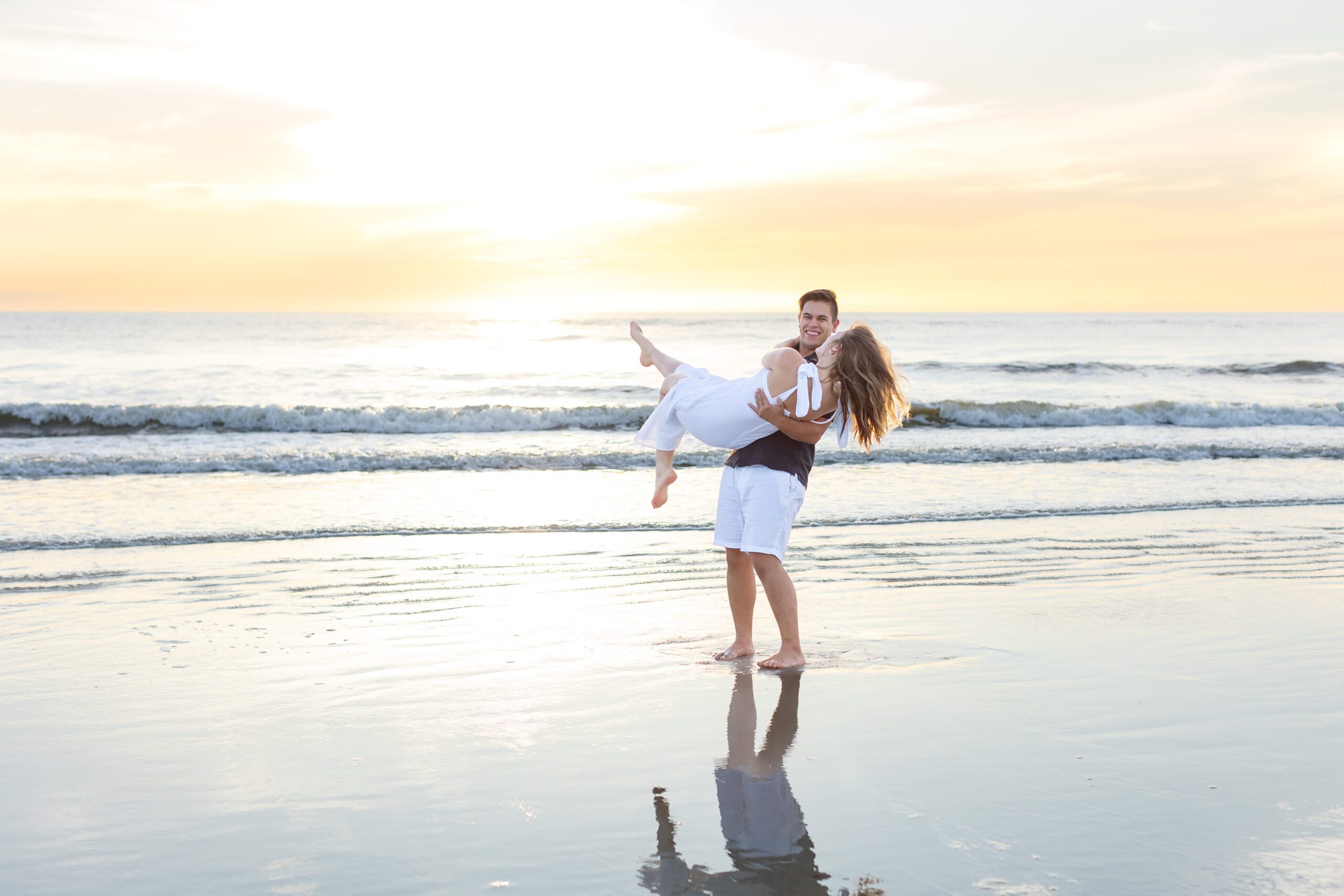 Guy lifts girl and spins her on the beach at sunrise for their engagement photos at New Smyrna Beach, Florida