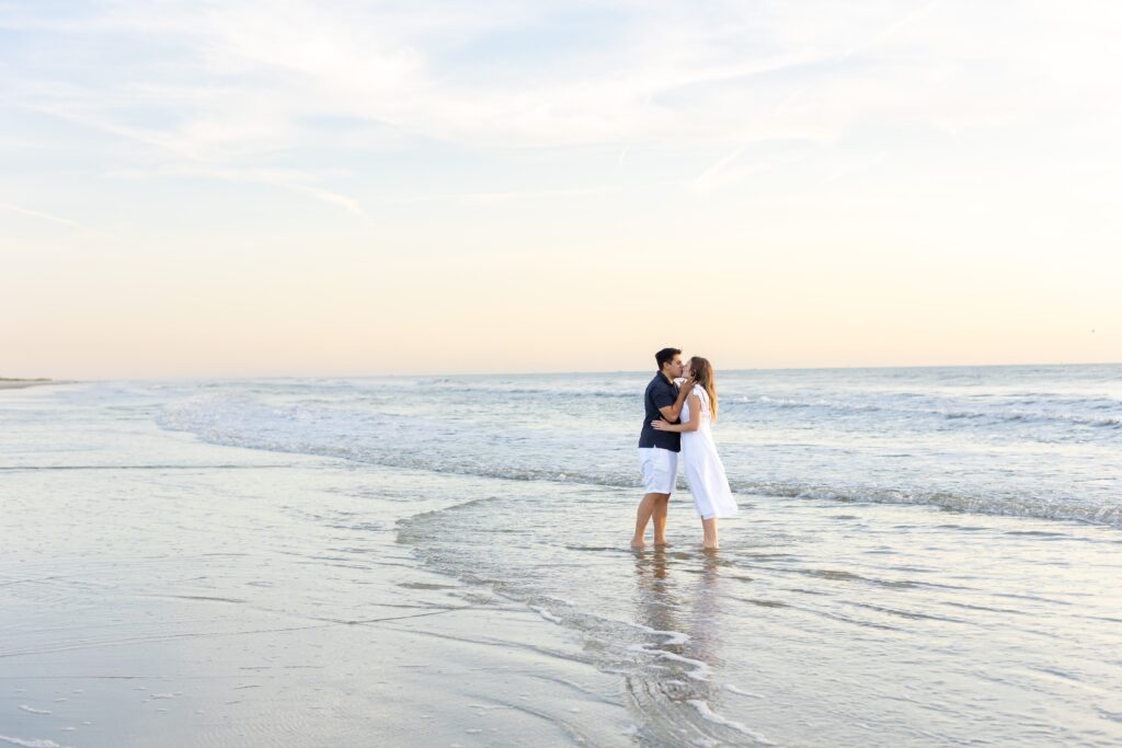 Couple kisses on the beach at sunrise for their engagement photos at New Smyrna Beach, Florida