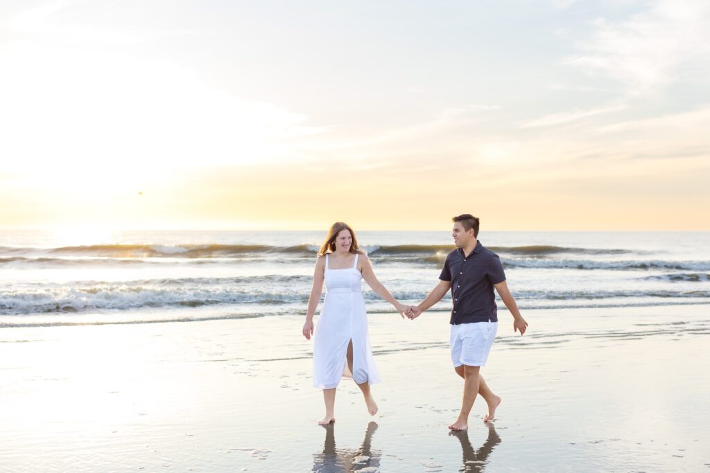 Couple walks and holds hands on the beach at sunrise for their engagement photos at New Smyrna Beach, Florida