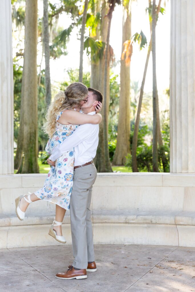 Guy lifts girl in front of Columns at Kraft Azalea Garden for their Winter Park Proposal