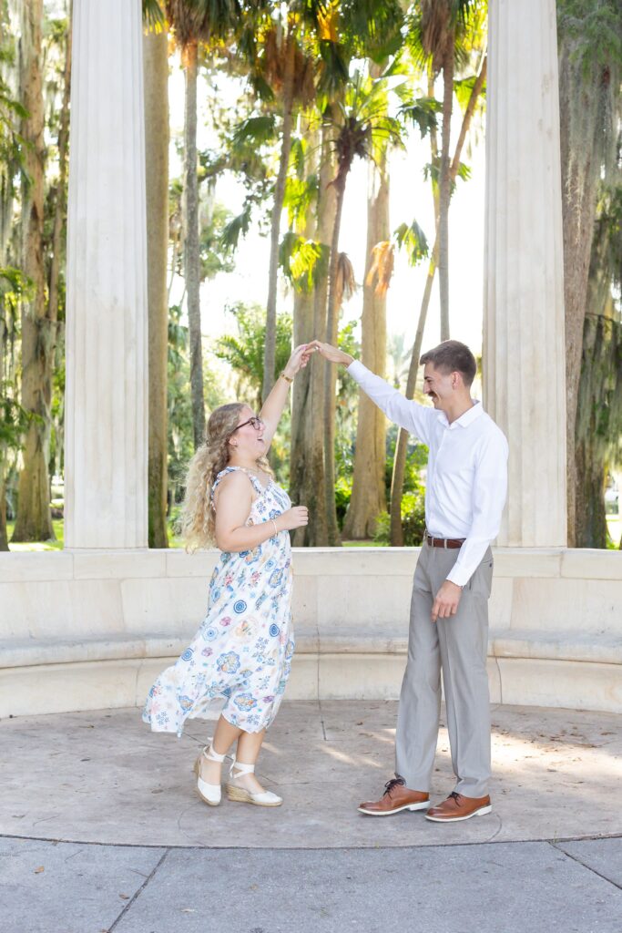 Guy twirls girl in front of Columns at Kraft Azalea Garden for their Winter Park Proposal